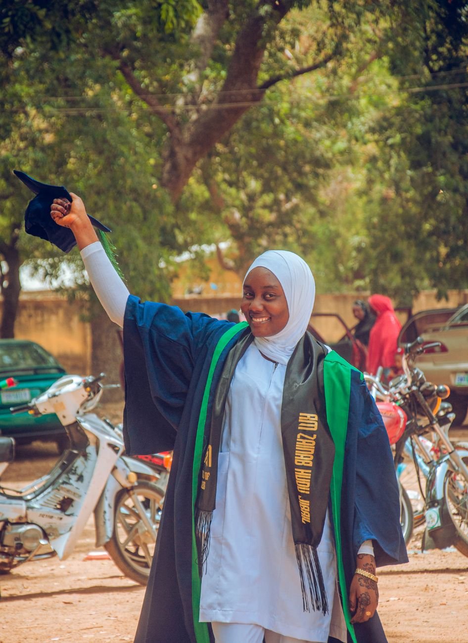 A cheerful female graduate celebrating her success in an outdoor ceremony, holding her cap high.